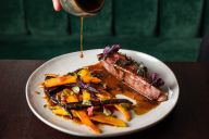 Dans un esprit plus décontracté, ce corner de restauration met en scène un comptoir élégant où s’alignent bocaux de produits maison, planches gourmandes et pâtisseries artisanales. Sur un plateau en marbre clair, les assiettes associent textures et couleu | © L'Almanach Montmartre