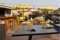 Perché sur le toit de l’immeuble, ce premier rooftop offre un espace convivial aux airs de lounge urbain. Banquettes aux coussins chatoyants, tables basses en métal et guirlandes lumineuses créent une ambiance festive, idéale pour des afterworks ou des év | © Mama Shelter Paris East