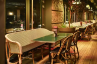 La terrasse, plus basse que les toits, propose un cadre semi-ouvert autour d’un bar central en zinc et de tabourets hauts. Plantes grimpantes et suspensions en rotin apportent une touche de verdure, tandis que les parasols colorés protègent du soleil pour | © Mama Shelter Paris East