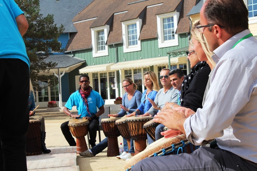 Groupe de salariés participant à un team building African Beats en extérieur sous la supervision d'un animateur.
