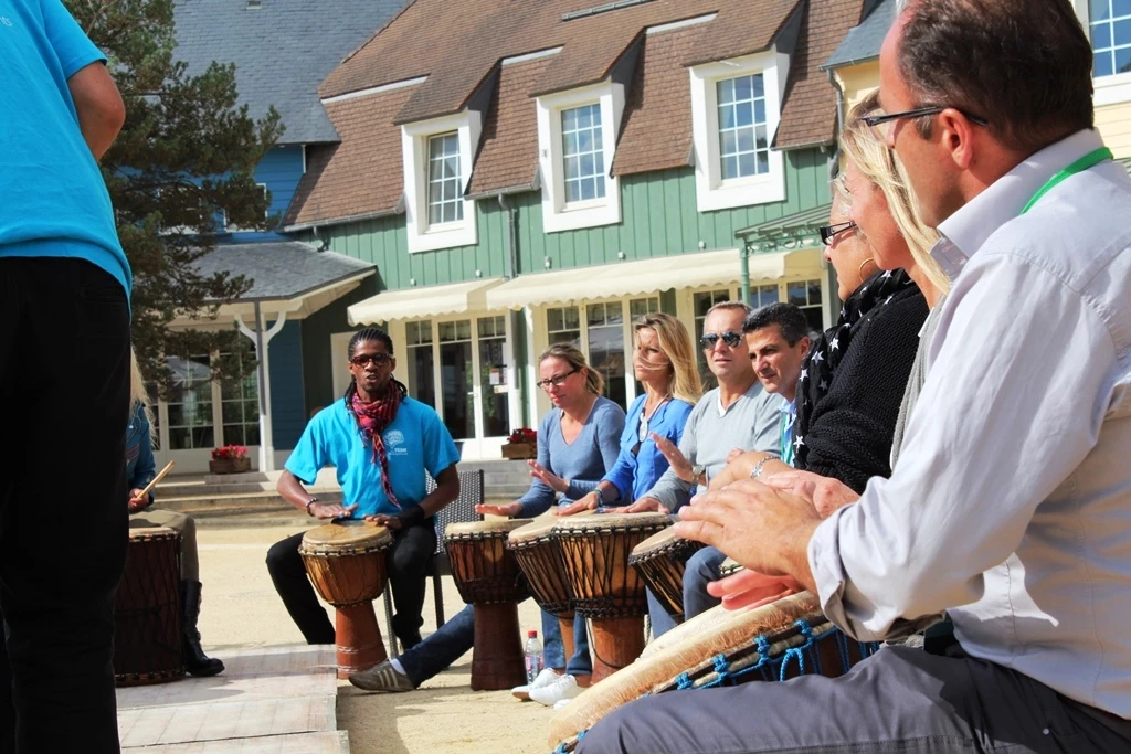 Groupe de salariés tapant sur des djembés en cercle sous le regard d'un animateur pendant un team building African Beats.
