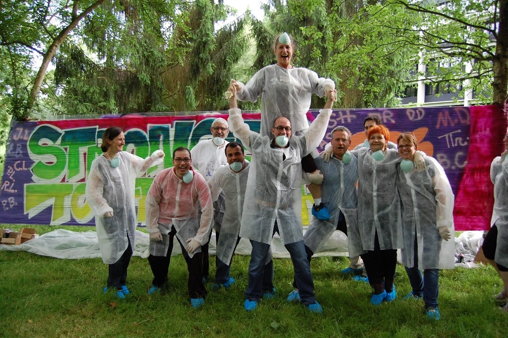 Groupe de collègues posant fièrement devant leur fresque collective lors d'un team building graffiti.